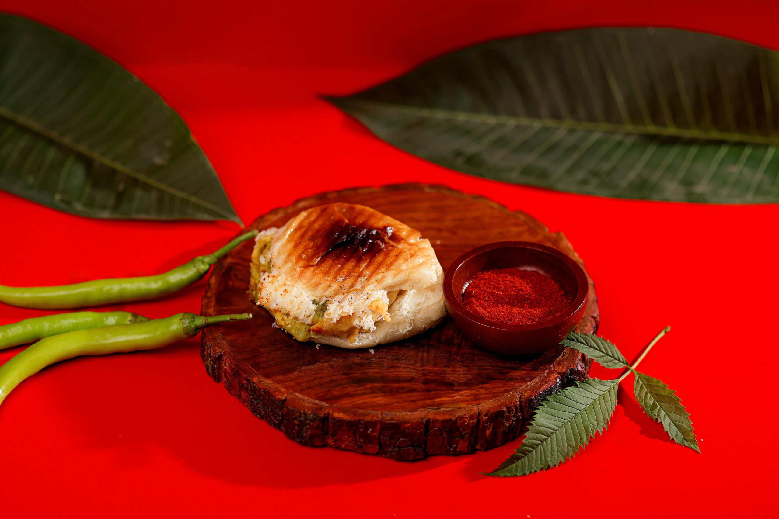 A grilled sandwich with spices on a wooden plate, set on a vibrant red background.